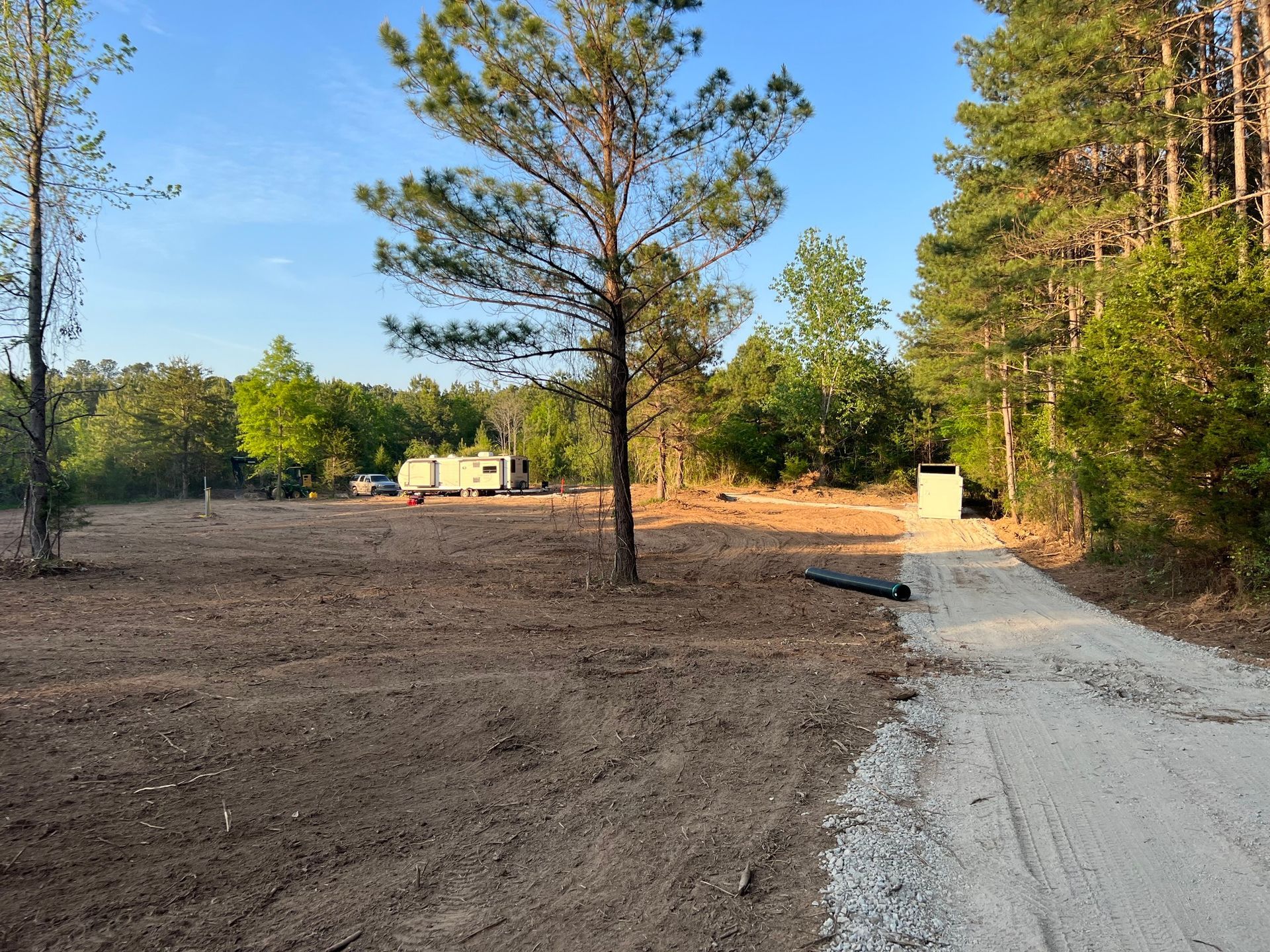 A dirt road leads to a cleared area with a trailer, trees, and a gravel drive.
