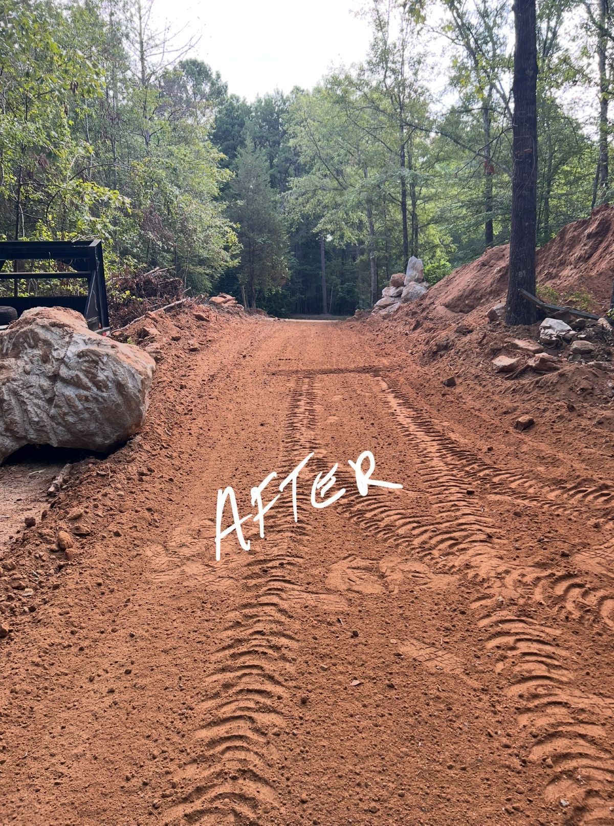 Dirt road, post-construction, with tire tracks. Trees and rock formations on sides.