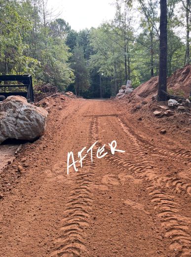 Dirt road, post-construction, with tire tracks. Trees and rock formations on sides. 