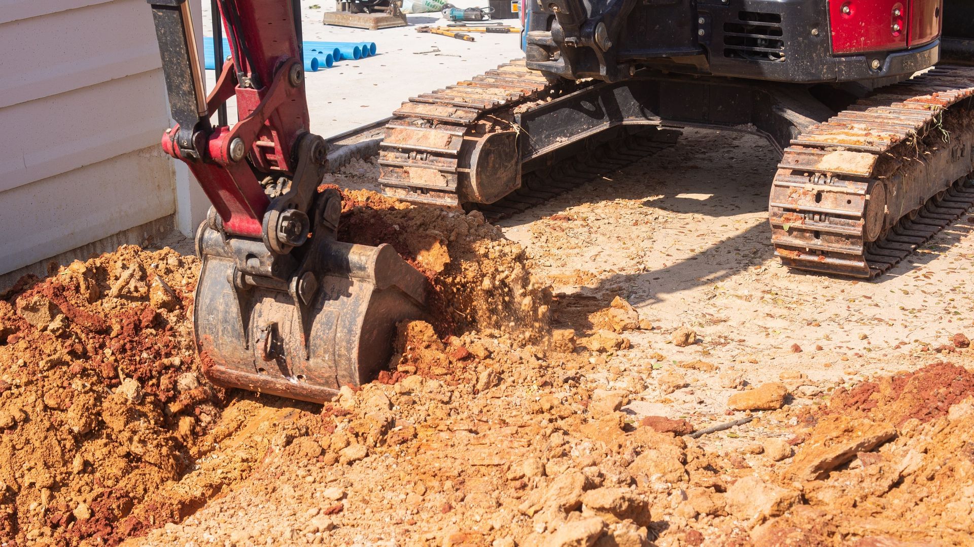 An excavator digging into the earth next to a building.
