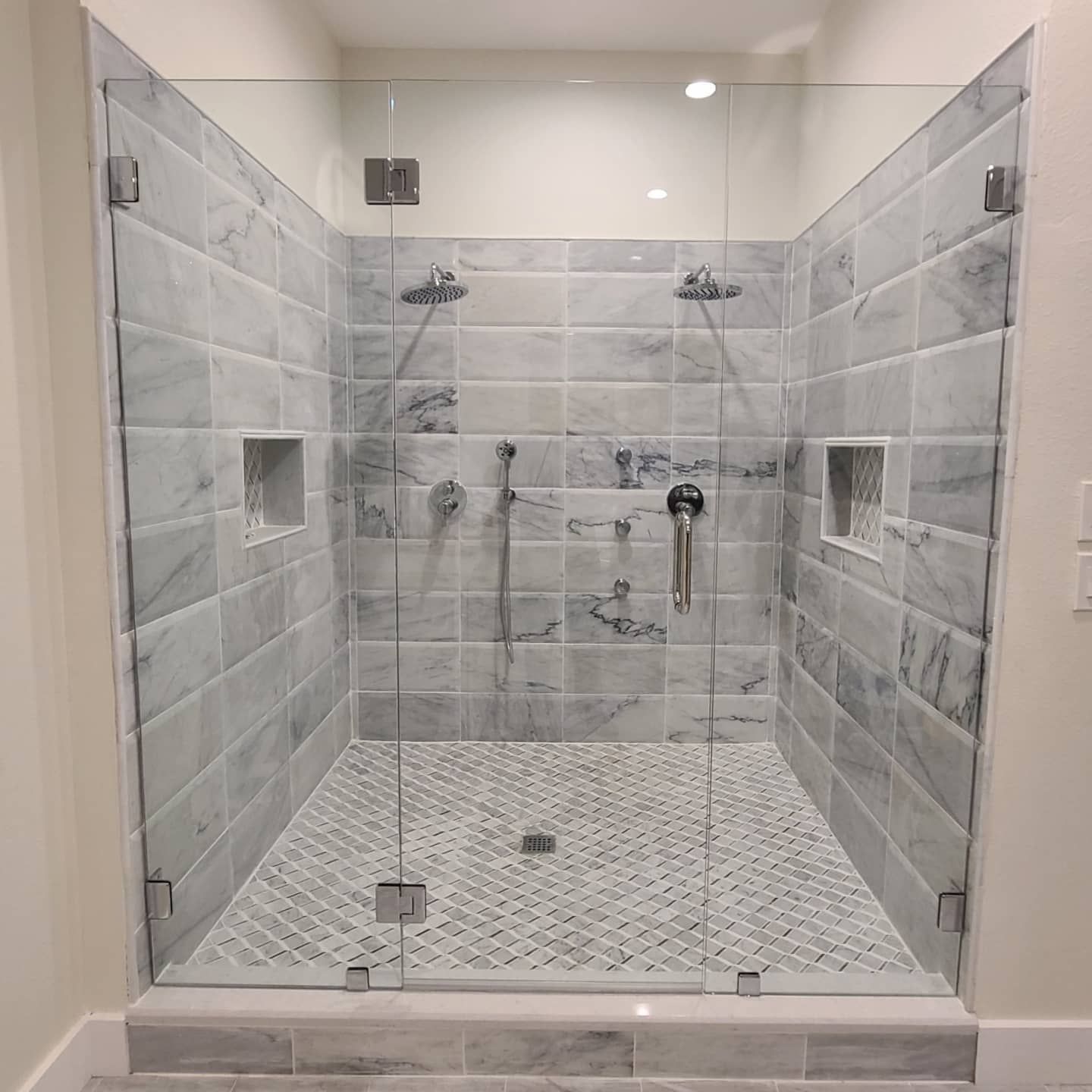 A bathroom with a walk in shower with marble tiles and a glass door.