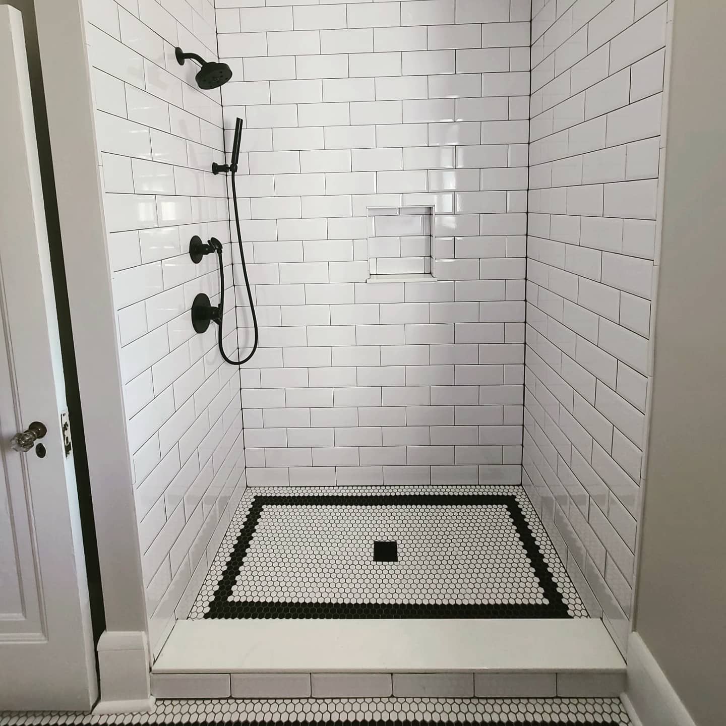 A shower with white brick walls and a black and white tile floor.