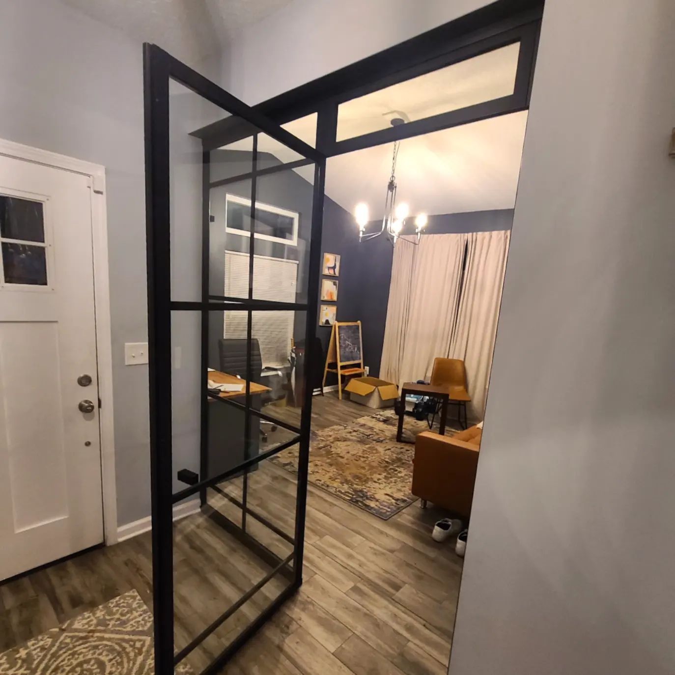 A living room with a glass door between the living room and the office