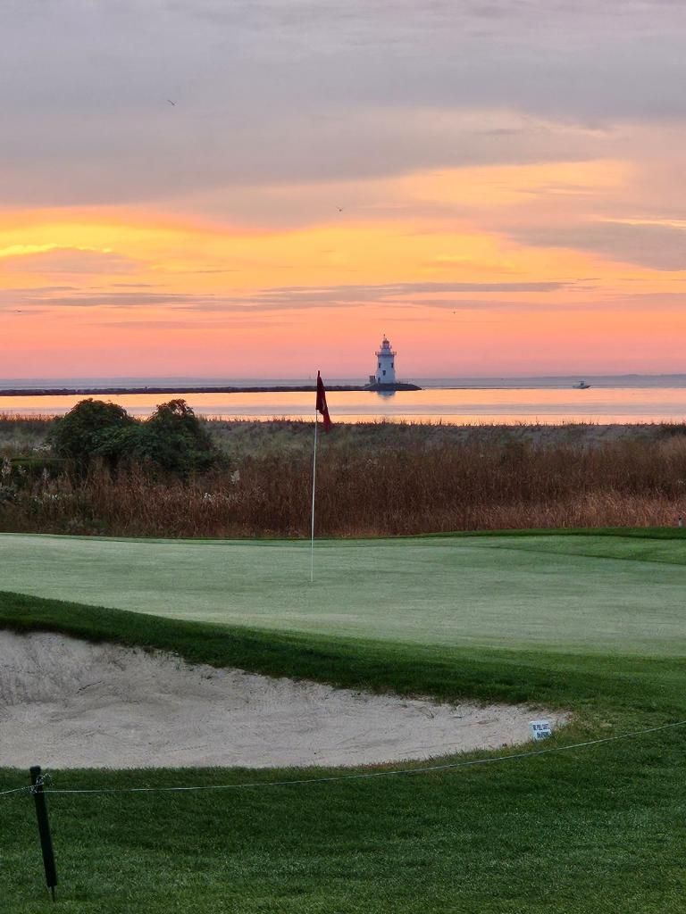 A golf course with a lighthouse in the background at sunset.