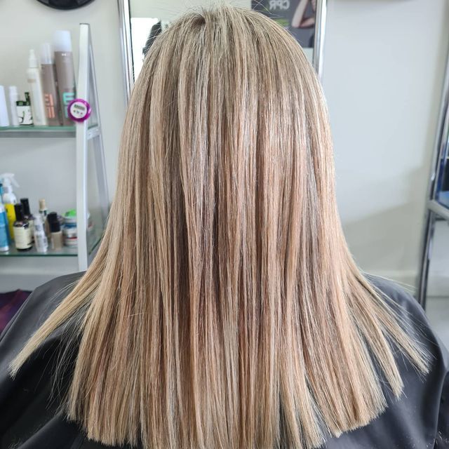 A Woman With Long Blonde Hair is Sitting in a Chair in Front of a Mirror — Lush Hair Studio in Tumbi Umbi, NSW