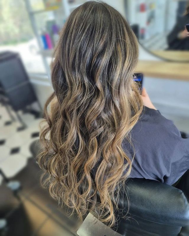 A Woman With Long Wavy Hair is Sitting in a Chair in a Salon — Lush Hair Studio in Tumbi Umbi, NSW