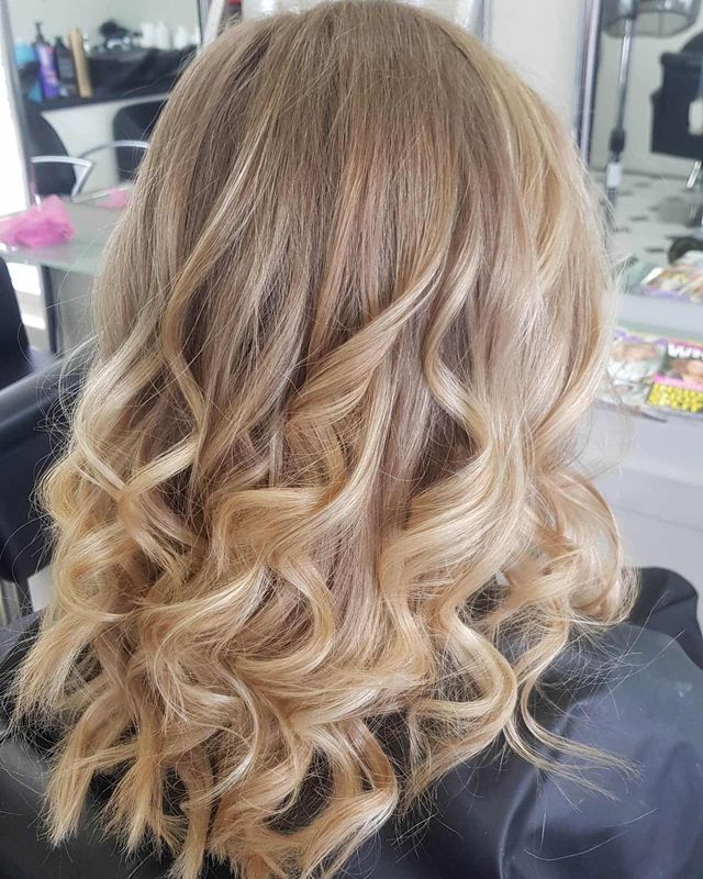 A Woman With Blonde Curly Hair is Sitting in a Chair in a Salon — Lush Hair Studio in Tumbi Umbi, NSW