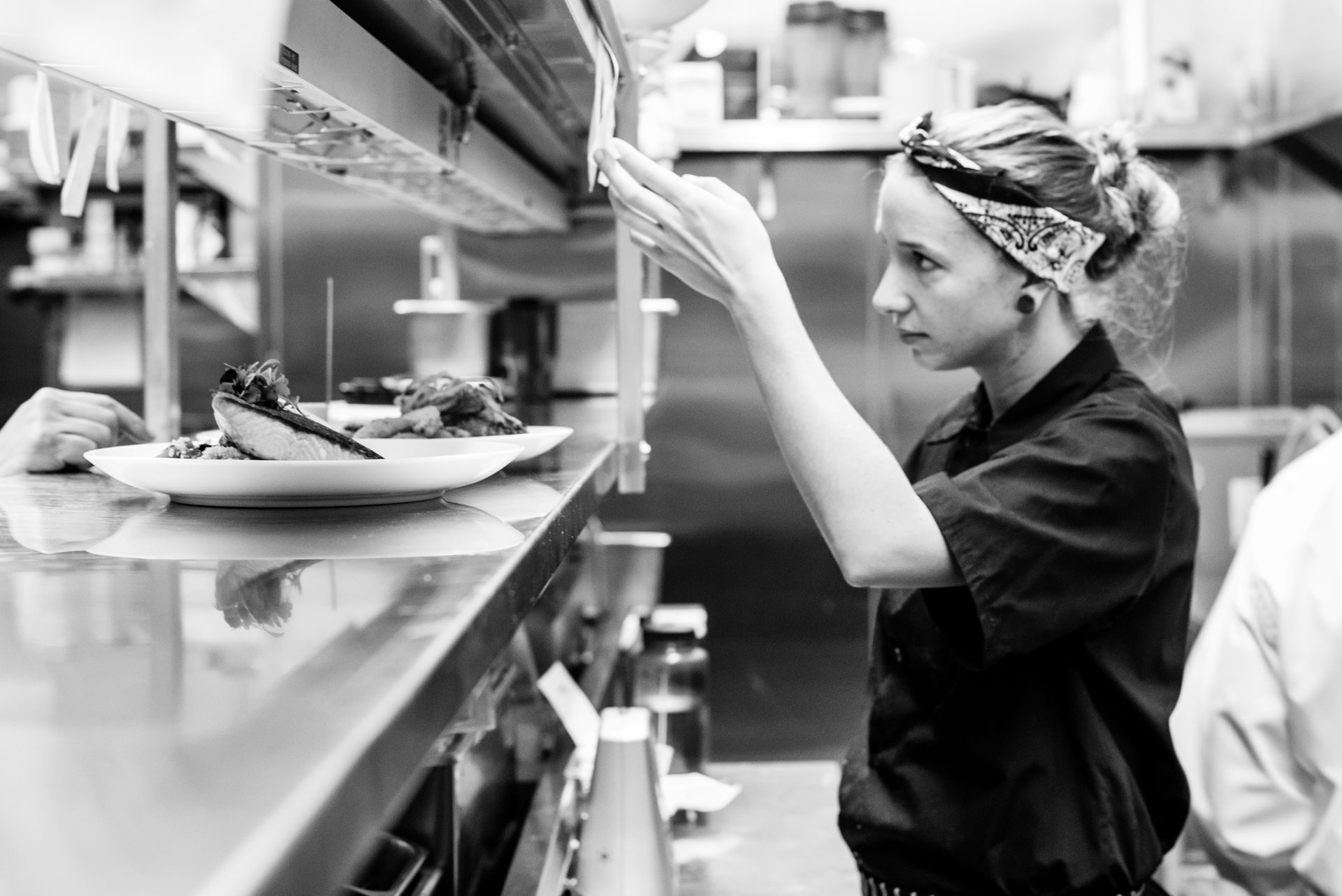 A woman is standing in a kitchen reaching for a plate of food.