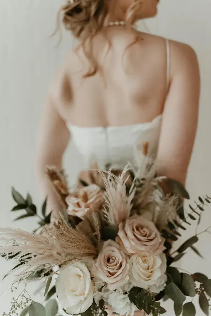 Bride in a white gown holding a bouquet of roses and pampas grass, back to the camera.