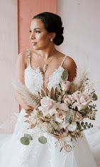Bride in a white dress holding a bouquet of blush-colored flowers and pampas grass, looking off to the side.