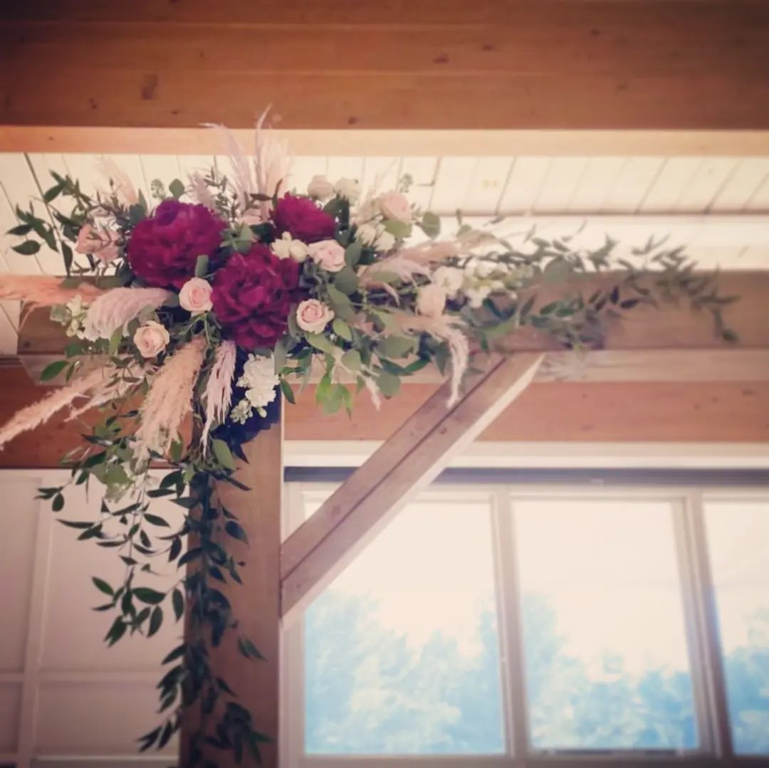 Floral arrangement on wooden beam with burgundy and blush flowers and greenery.