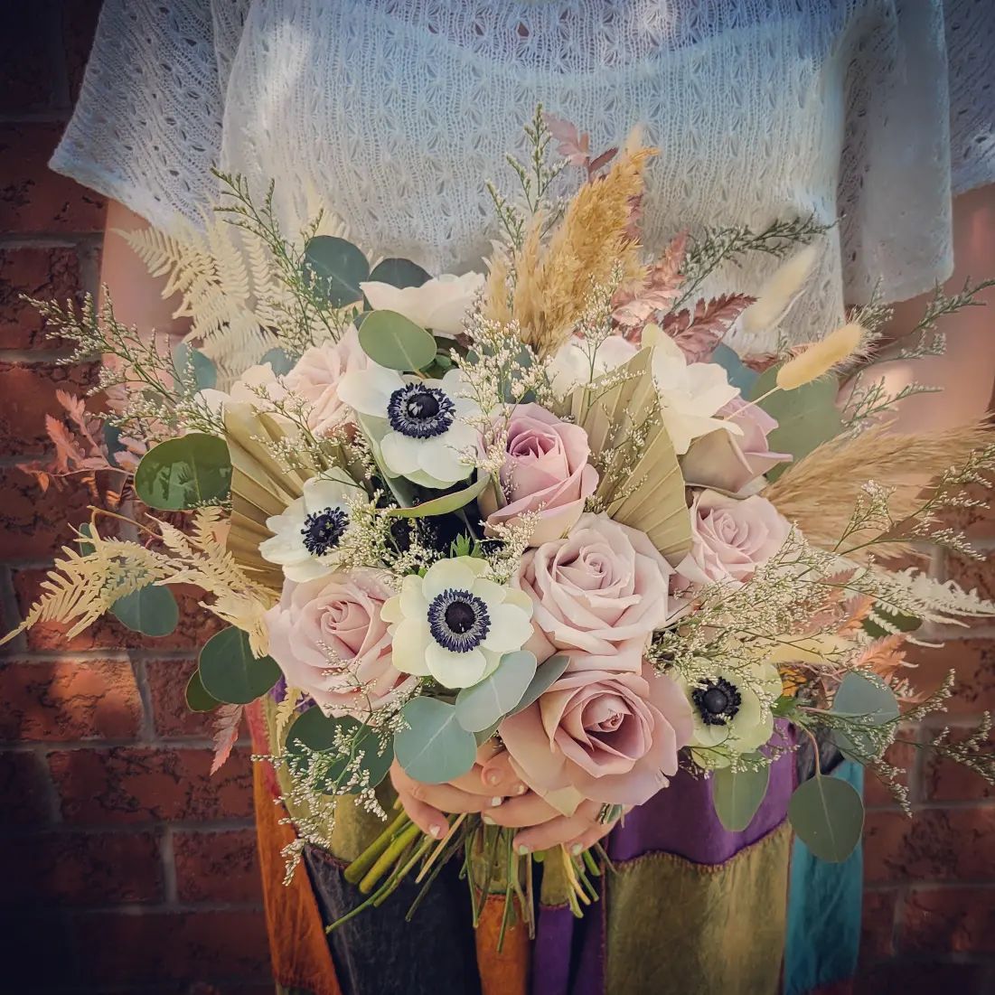 Woman holding a bouquet of pink roses, white anemones, and dried grasses.