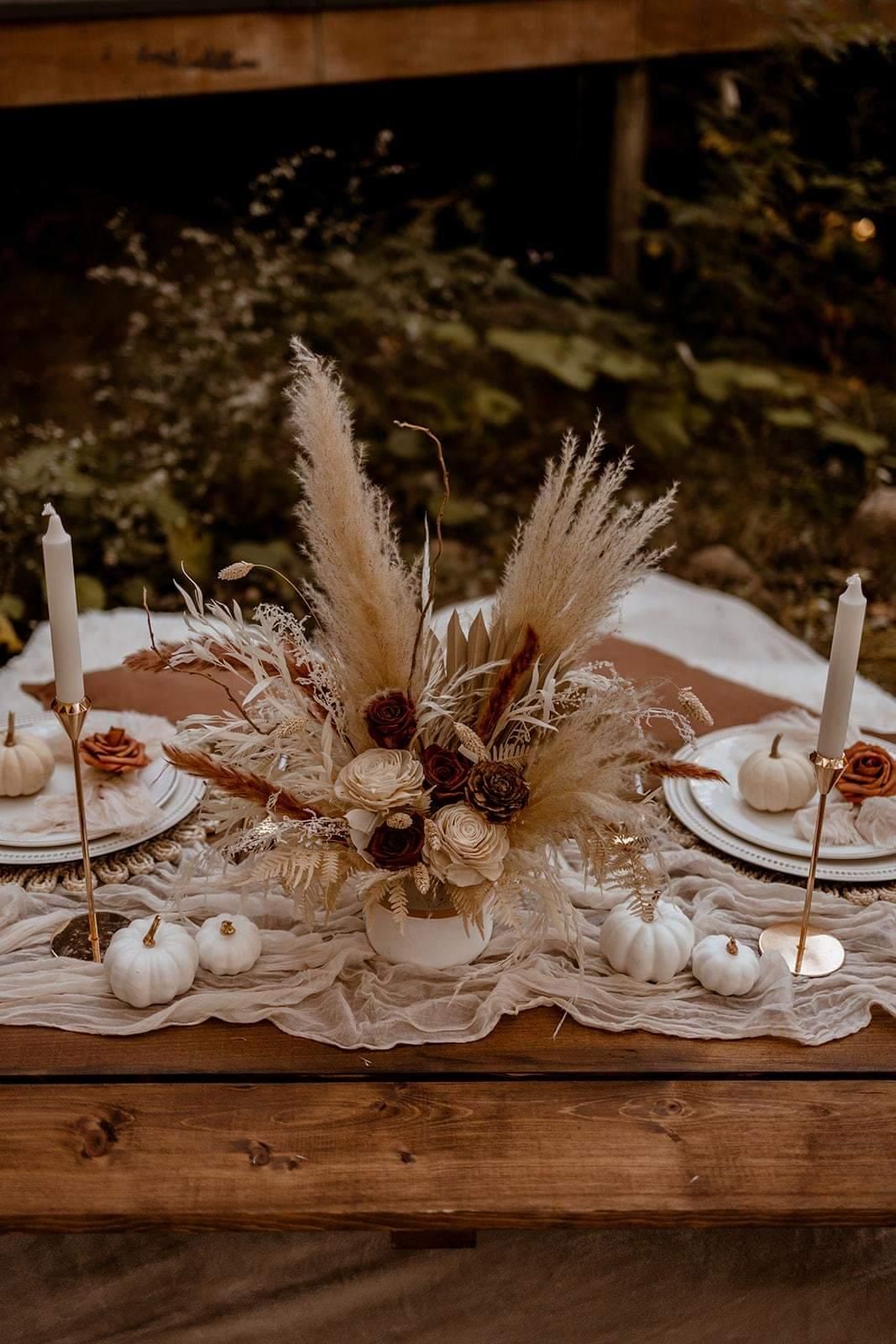 Fall-themed table setting: center floral arrangement, pumpkins, candles, neutral tones, outdoor setting.