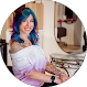 Woman with blue hair, tattoos, and off-the-shoulder shirt smiling, likely inside, with a mirror behind her.