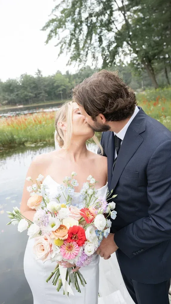 Bride and groom kissing on a dock, holding flowers.