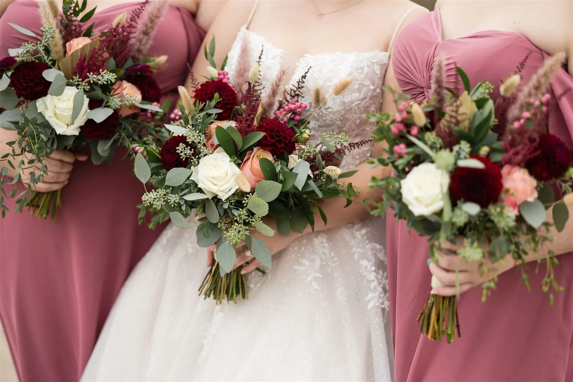 Bride and bridesmaids with bouquets. The bride wears a white gown, the bridesmaids wear dresses and hold floral bouquets.