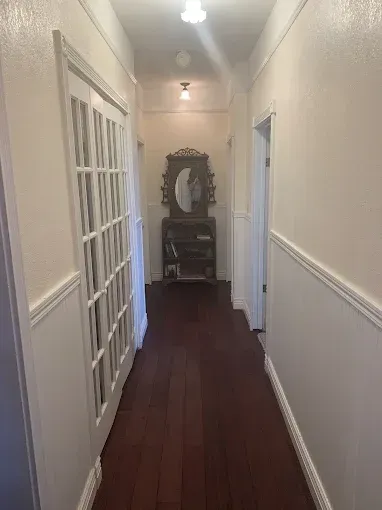Narrow hallway with dark wood floor, white wainscoting, and a mirrored dresser at the end.