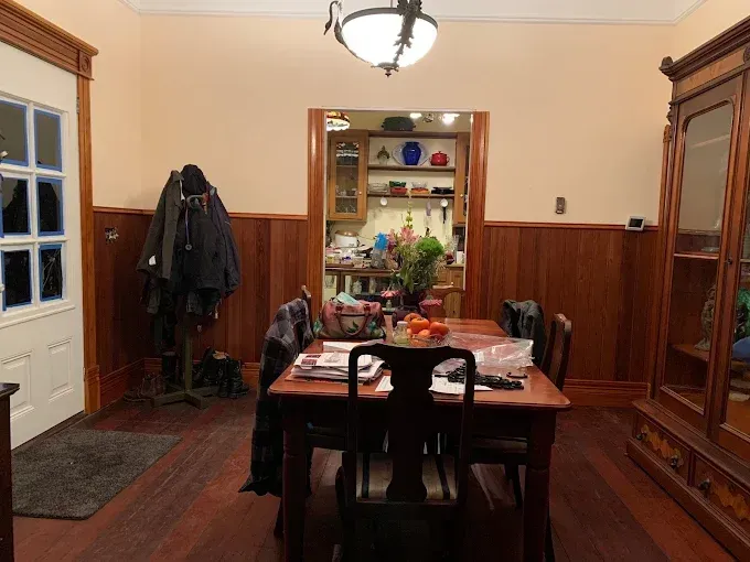 A dining room with a table, chairs, a doorway to the kitchen, and a wooden cabinet.