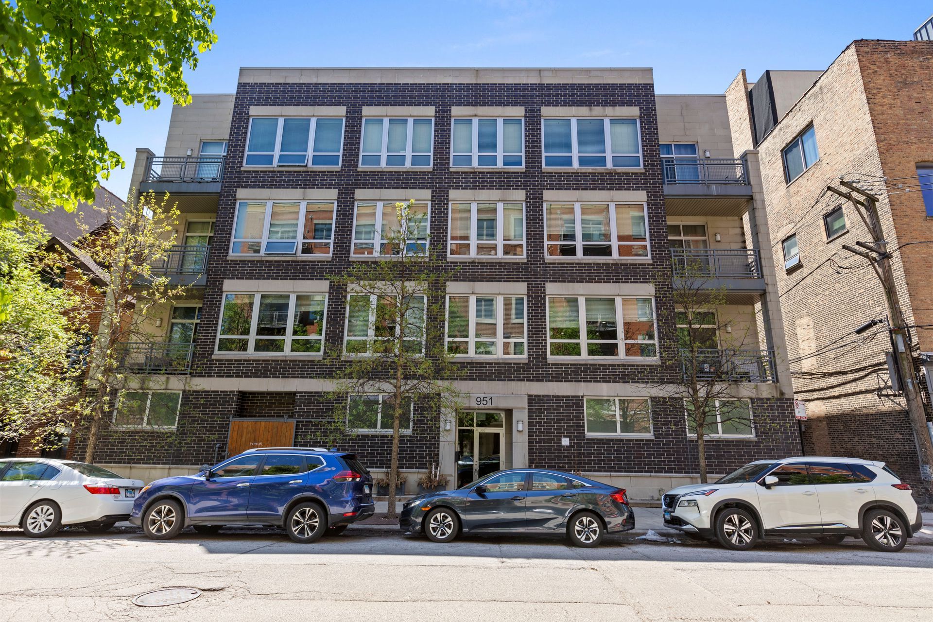 A row of cars are parked in front of a large brick building.