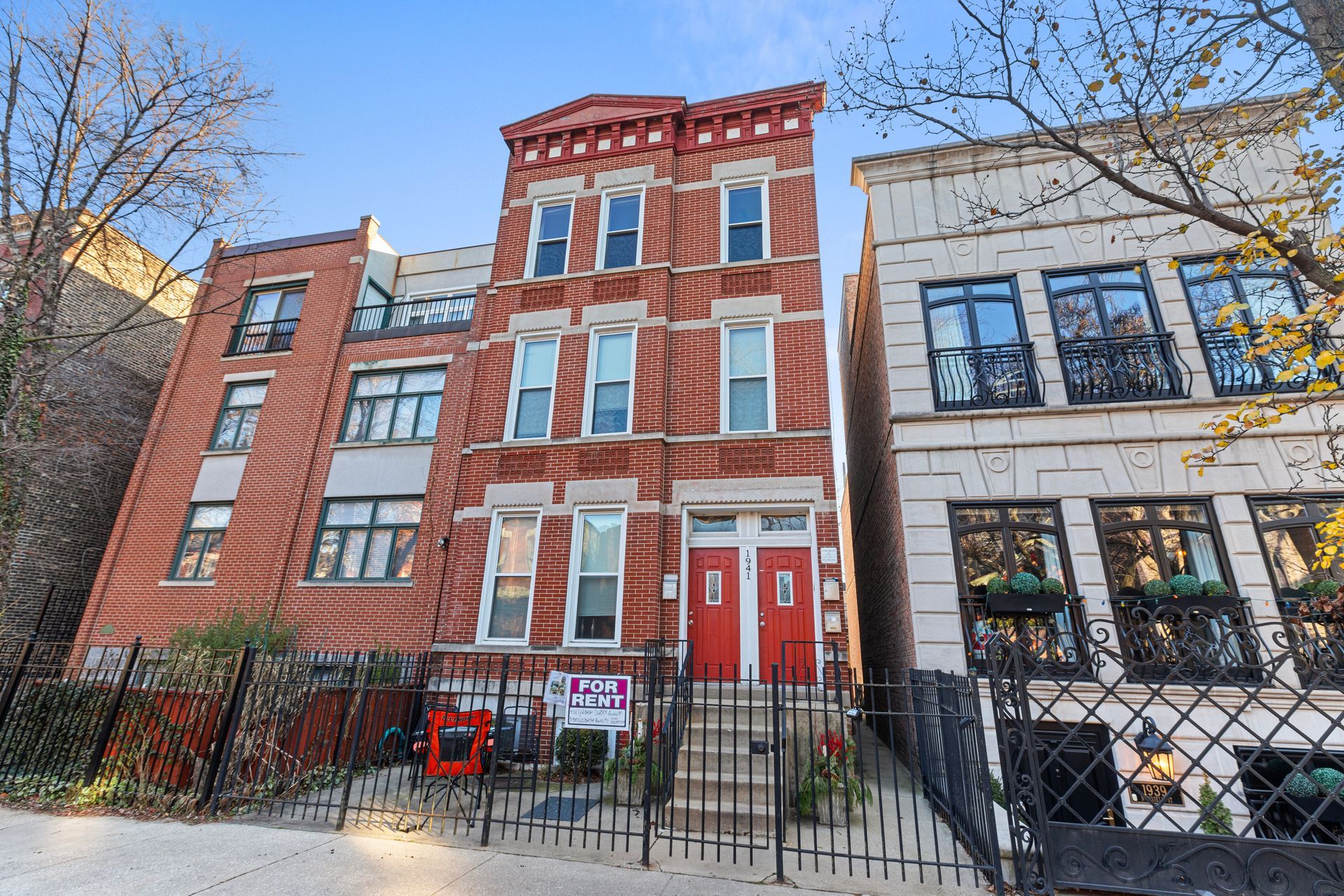 A brick building with a red door is next to a white building