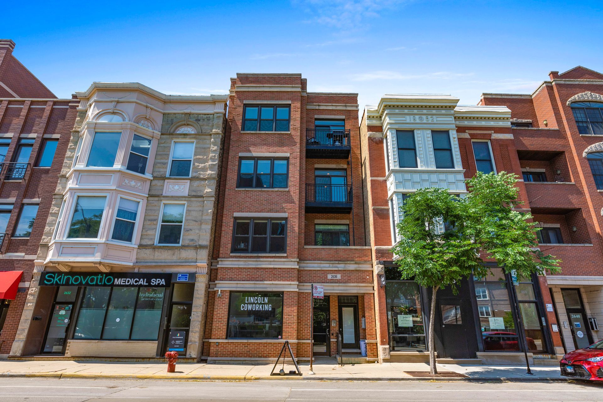 A red car is parked in front of a row of brick buildings.