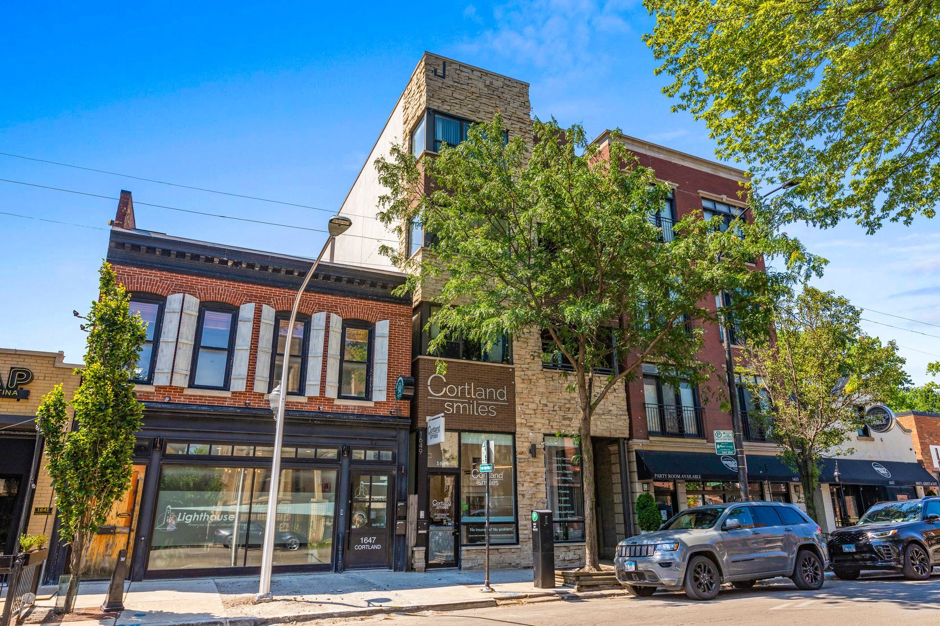 A row of buildings on a city street with cars parked in front of them.