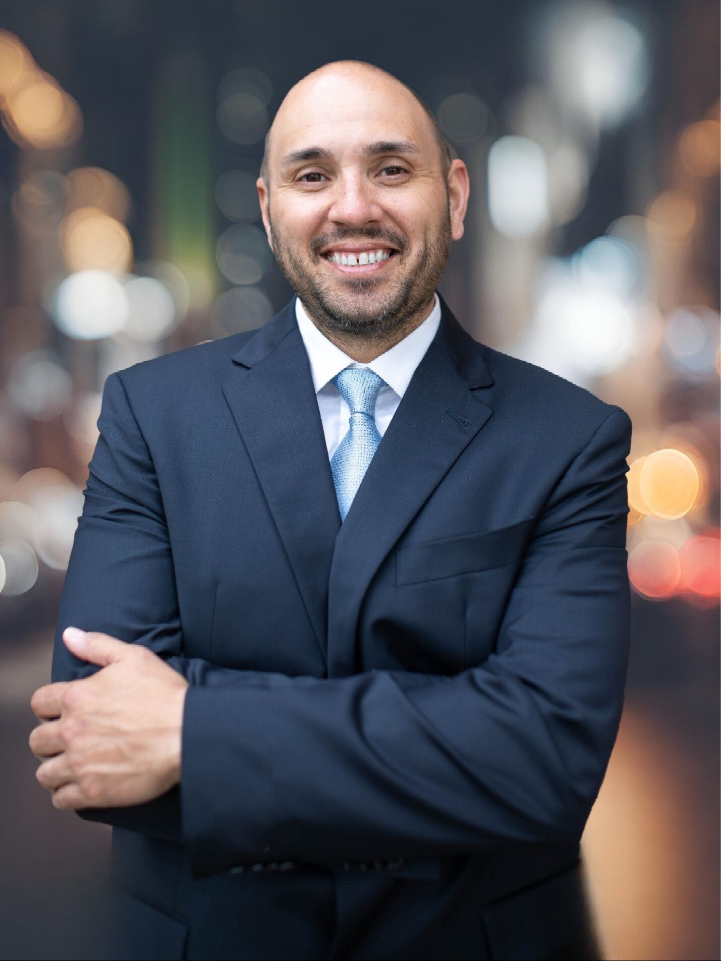 A man in a suit and tie is standing with his arms crossed.