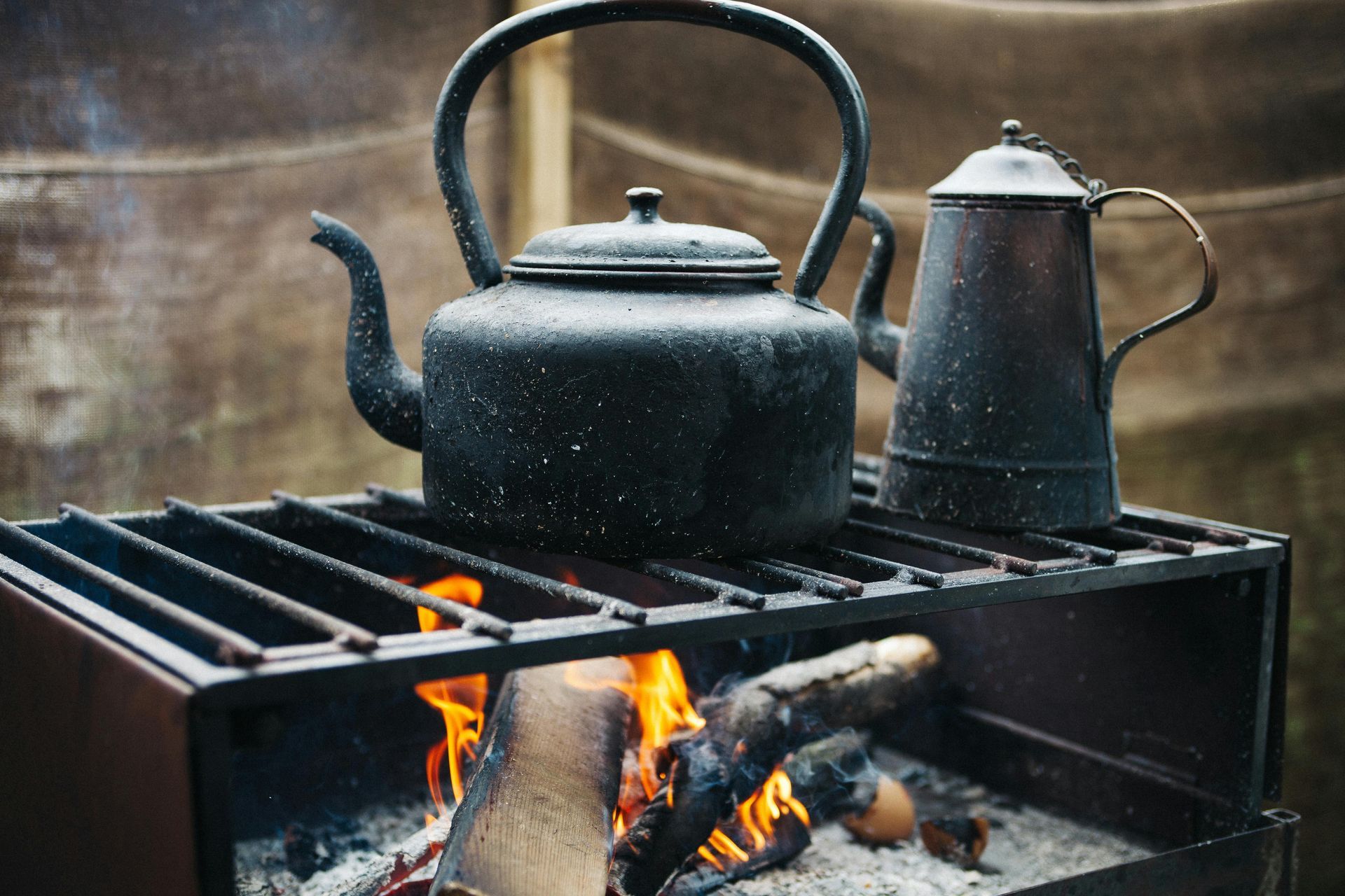 Black kettle and coffee pot on a grill over a burning campfire.