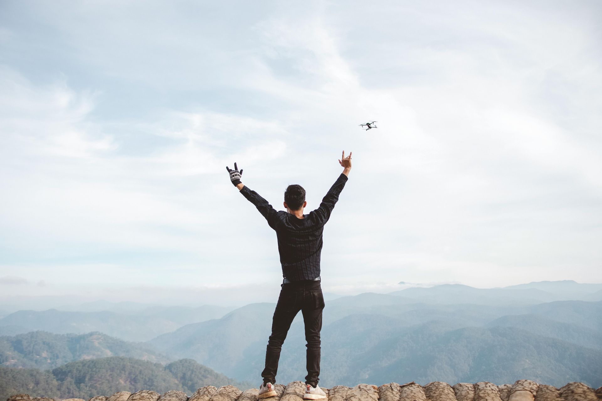 Man with arms raised on a mountain, a drone flies above.