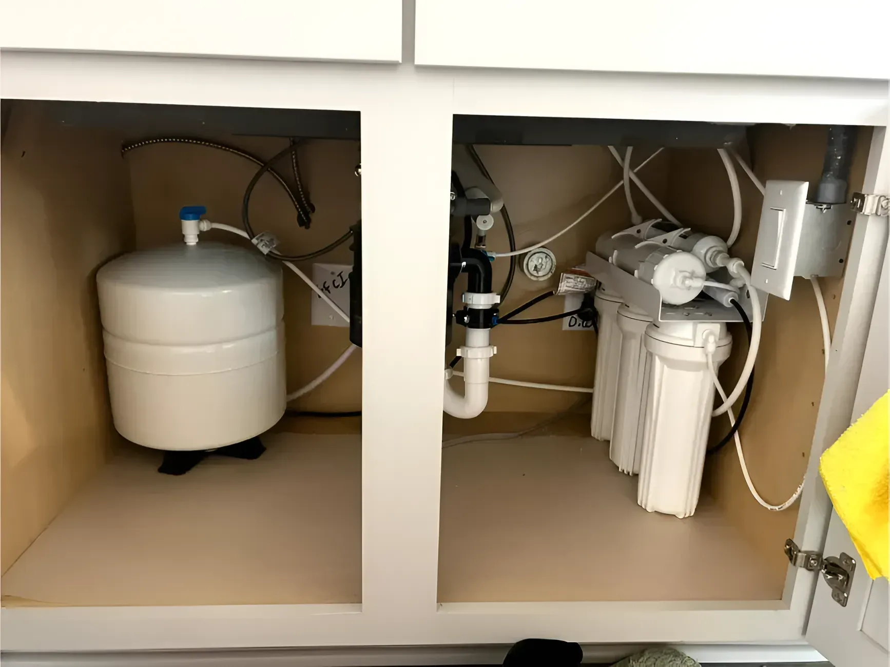 Under-sink reverse osmosis water filter system in a kitchen cabinet, showing tank and filter cartridges.