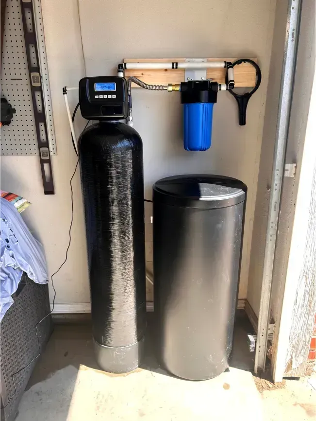 Water filtration system in a garage, including a black tank with a digital display, a blue filter, and a salt tank.