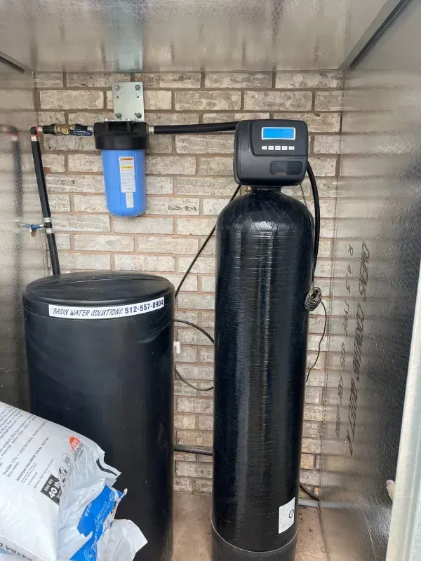 Water filtration system with blue filter, black tank, and control panel on a brick wall.
