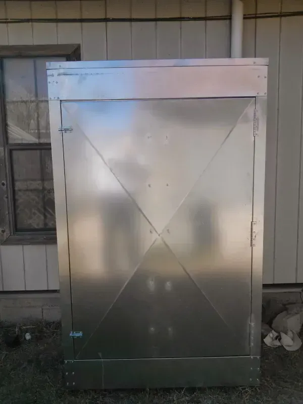 Large, shiny, metallic box-like structure outdoors next to a building; could be an HVAC unit.