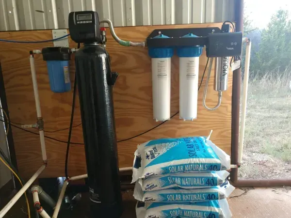 Water filtration system with various filters, a salt tank, and bags of salt against a wooden wall.