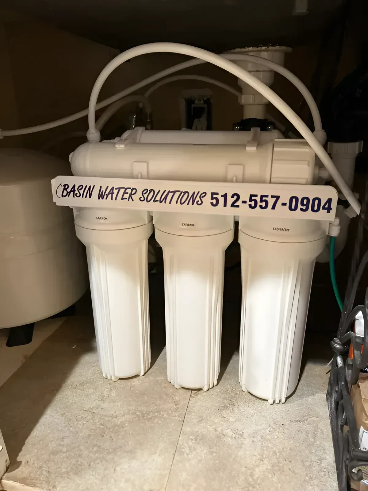 White water filter system with three canisters, a tank, and plumbing under a counter.