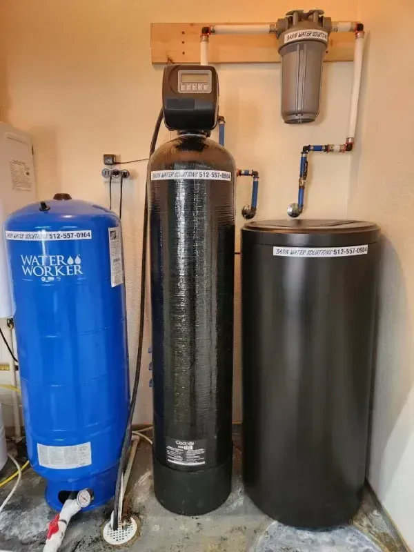 Water softener system: blue tank, black cylinder with control panel, black brine tank, and filter on a wall.