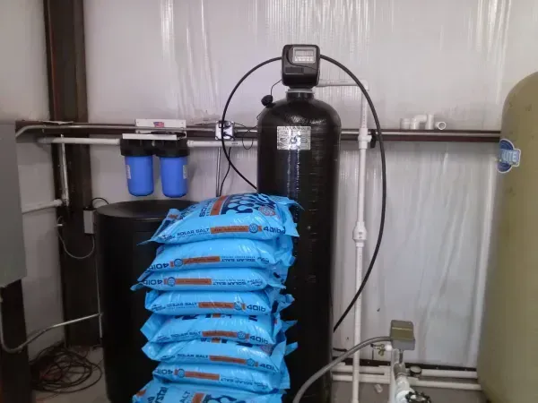 Water filtration system with black tanks, blue filters, and a stack of salt bags.