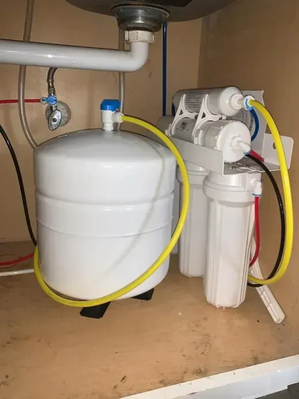 Under-sink reverse osmosis water filtration system with a white storage tank and multiple filter cartridges connected by tubes.