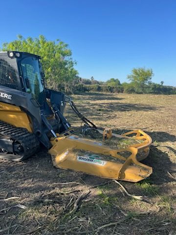 Yellow skid steer with brush cutter on dry field under trees
