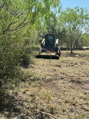 Yellow excavator digging red dirt on a rural construction site with trees nearby