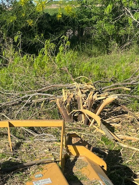 Yellow brush-clearing machine pushing a pile of branches in a grassy field