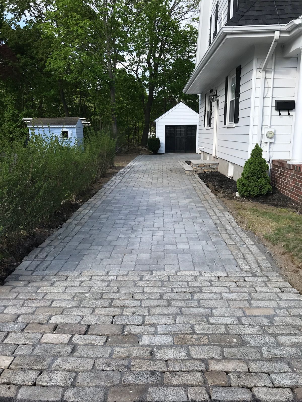 A cobblestone driveway leading to a white house.