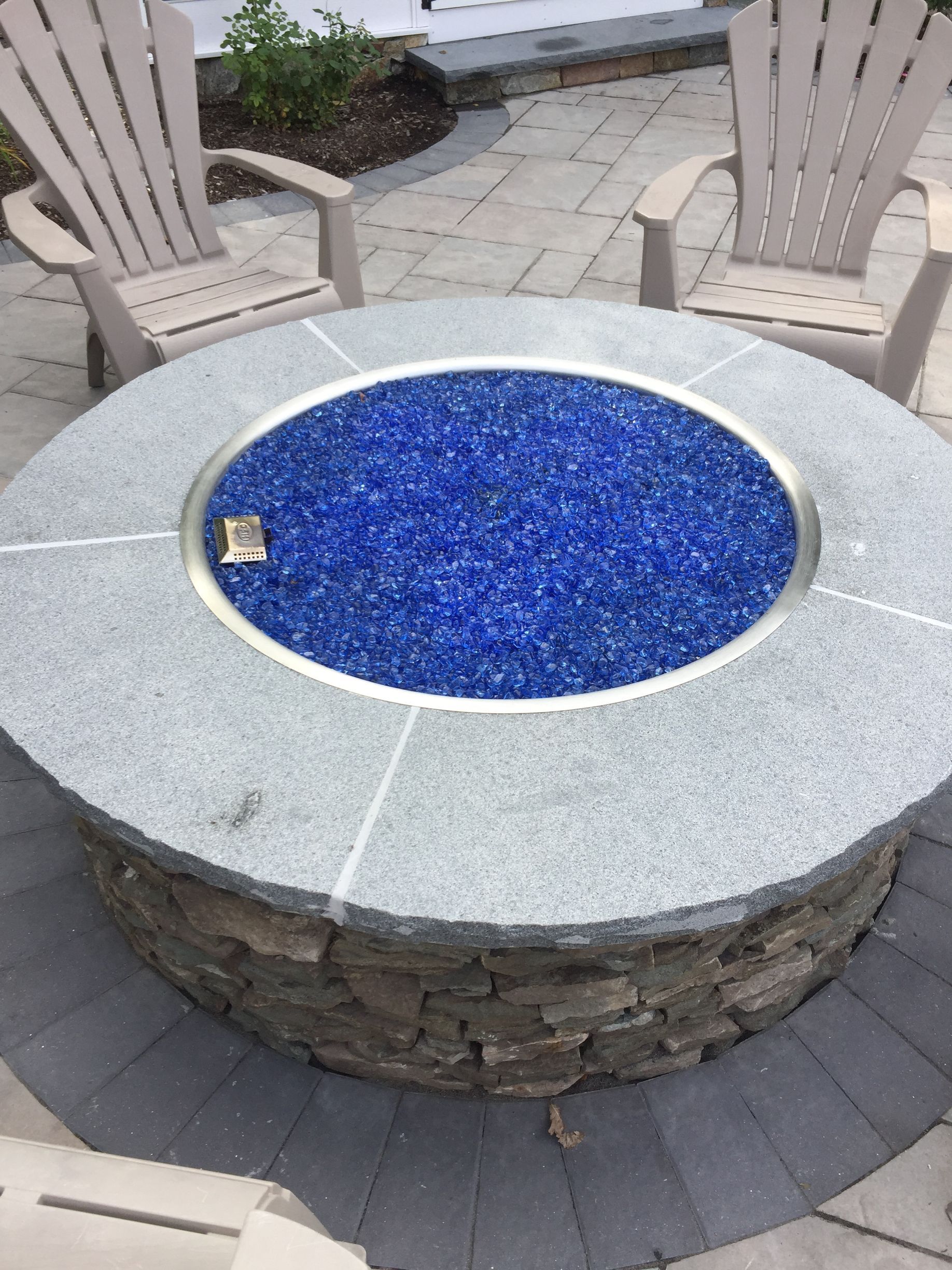 A fire pit surrounded by chairs on a patio with blue glass in it.