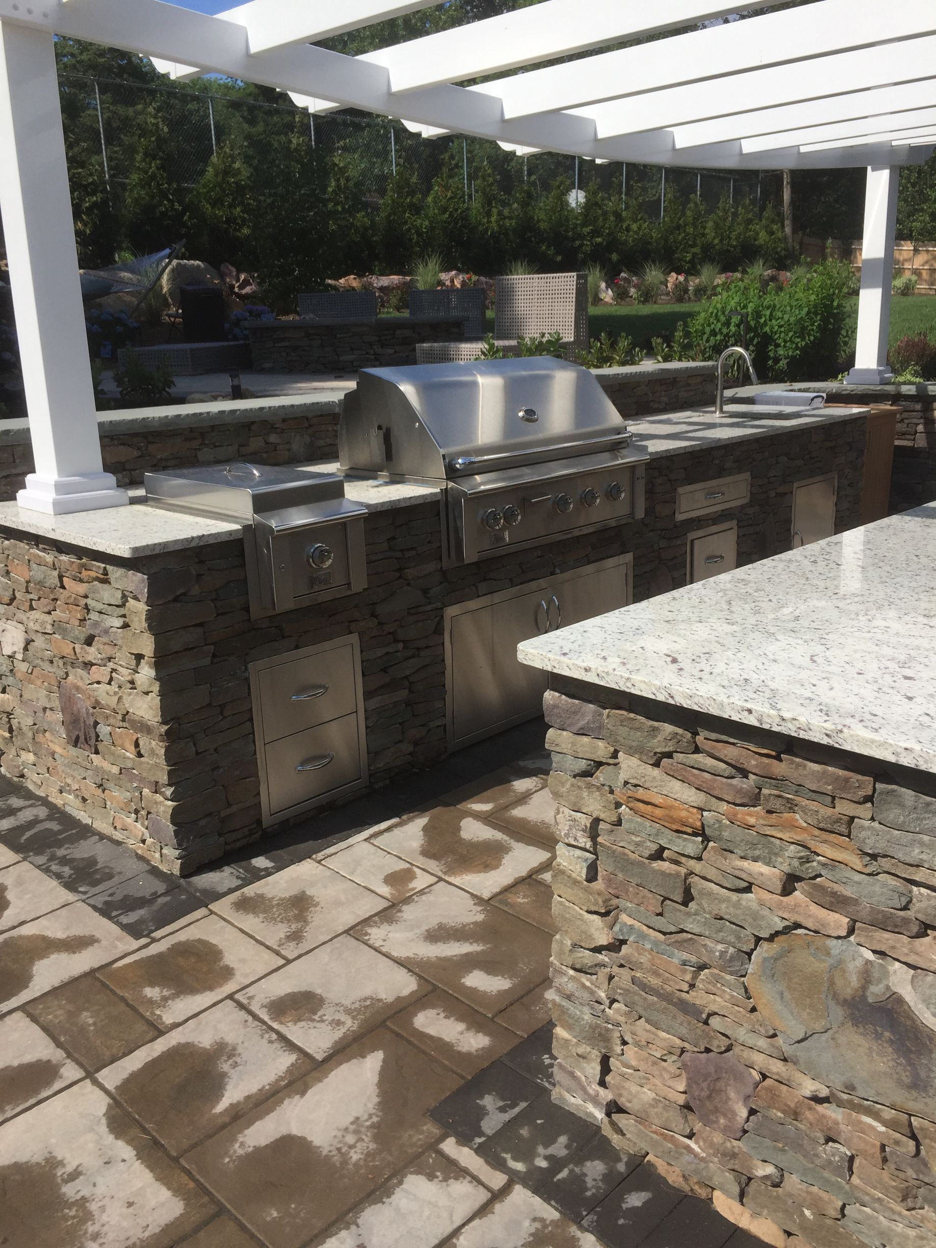 An outdoor kitchen with a stainless steel grill and granite counter tops