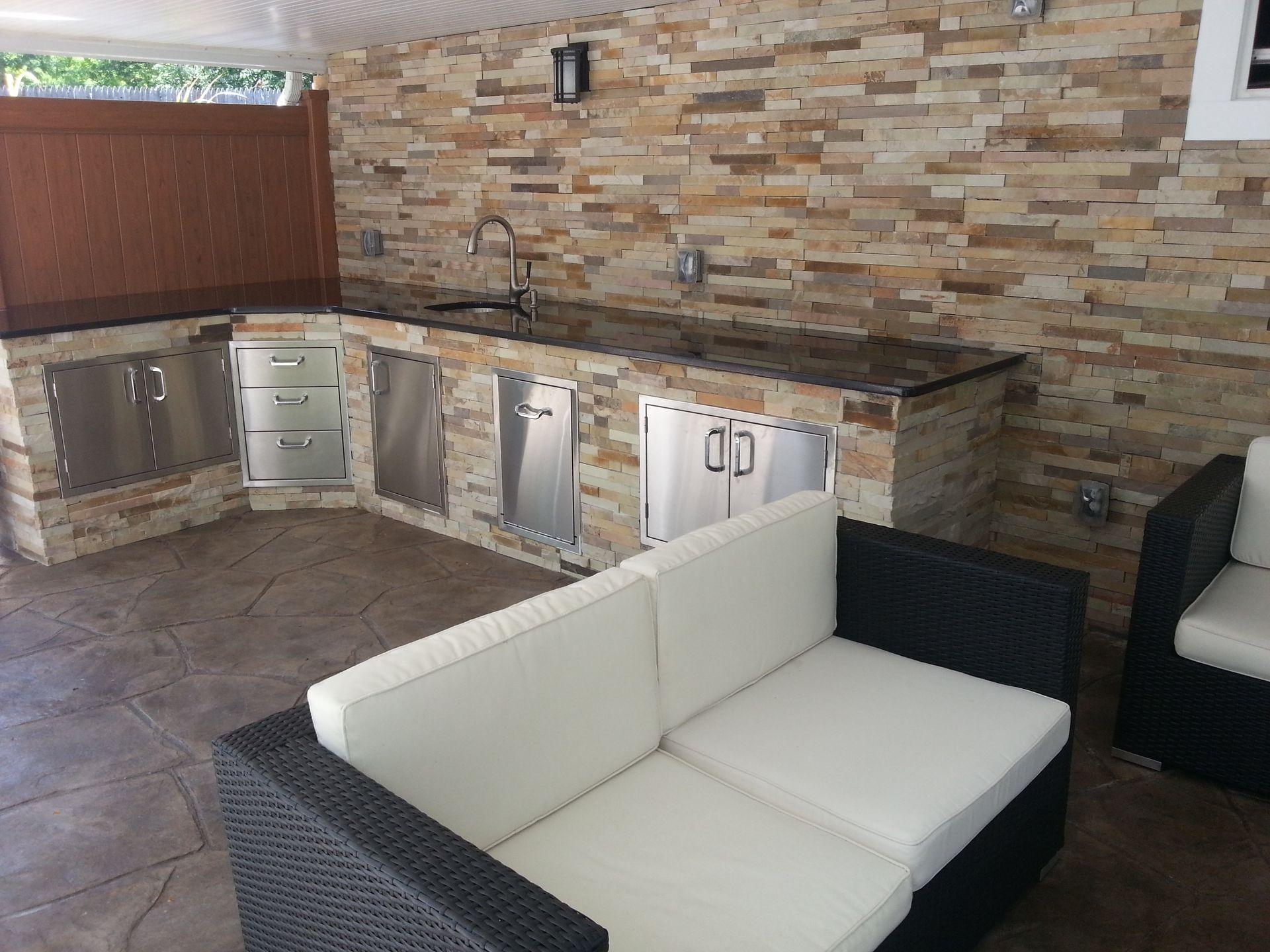 A patio area with a couch and chairs in front of a stone wall