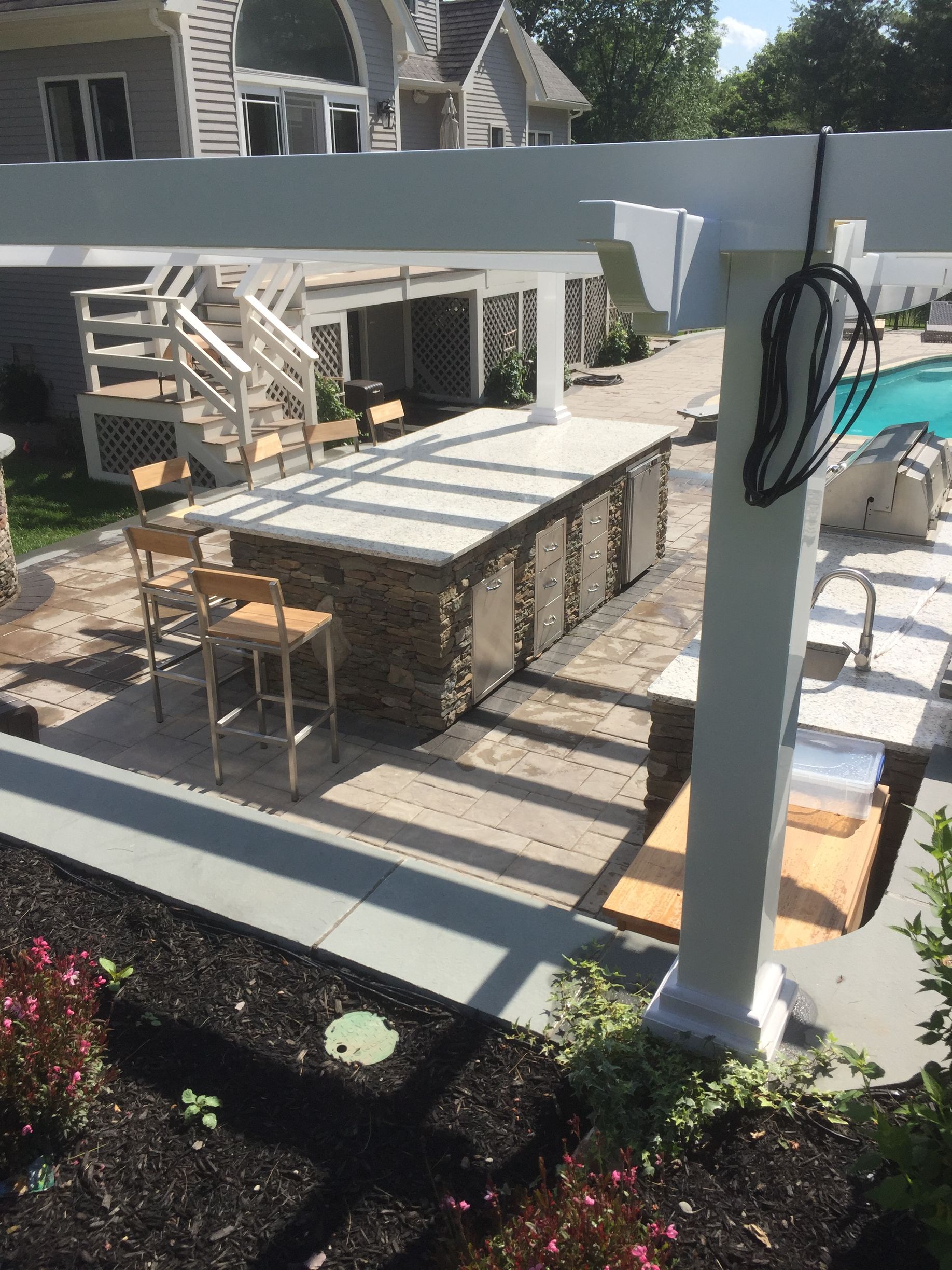A patio area with a pergola and a swimming pool in the background.