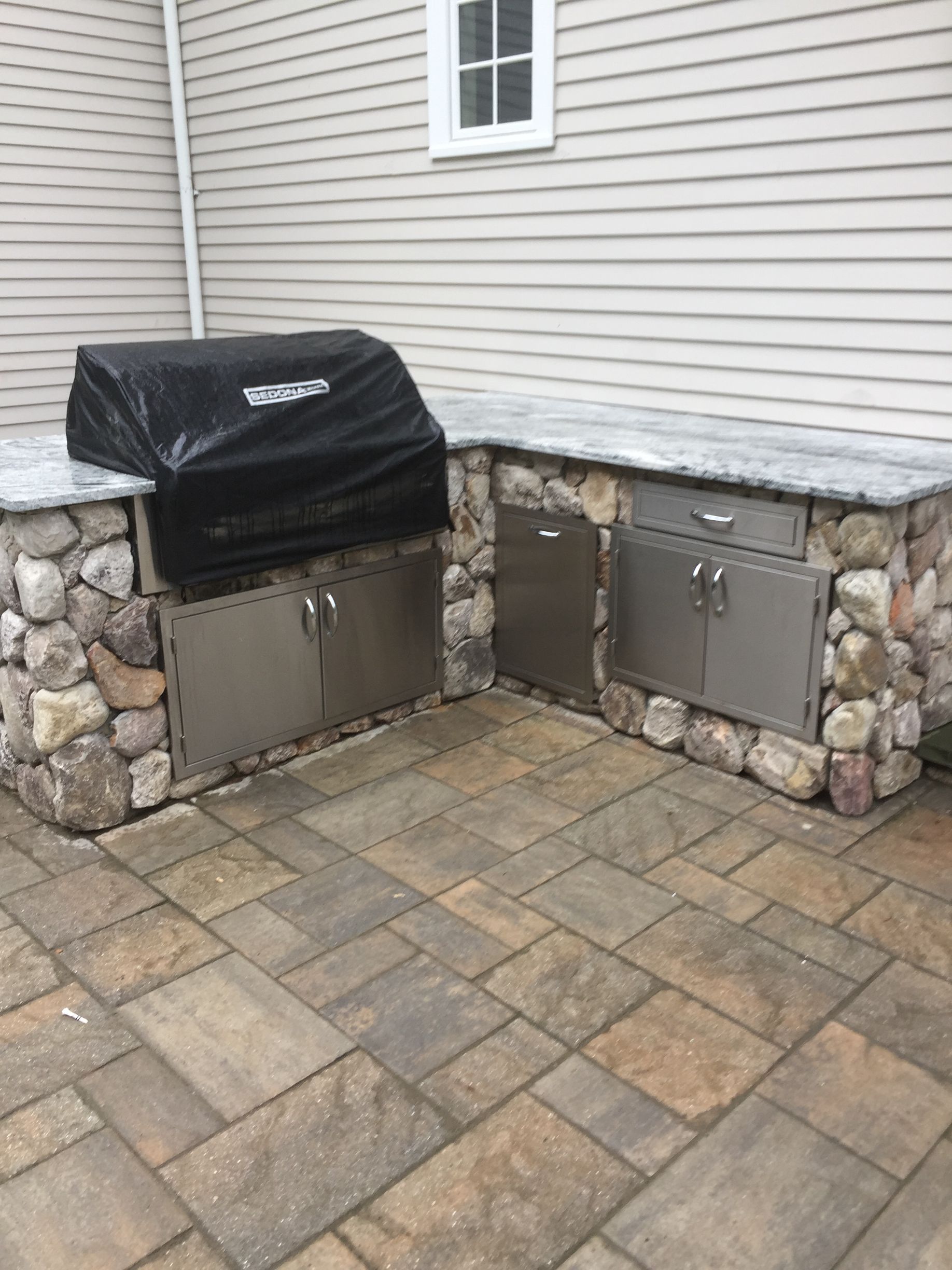 A grill is sitting on top of a stone patio next to a house.