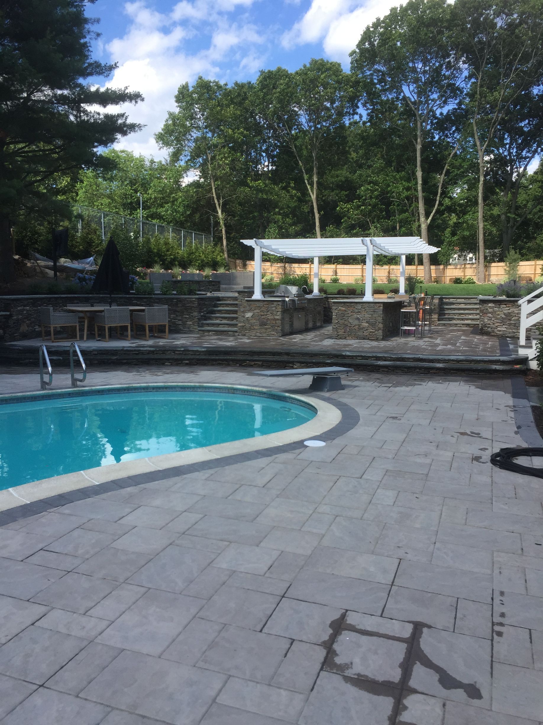 A large swimming pool is surrounded by trees and a pergola