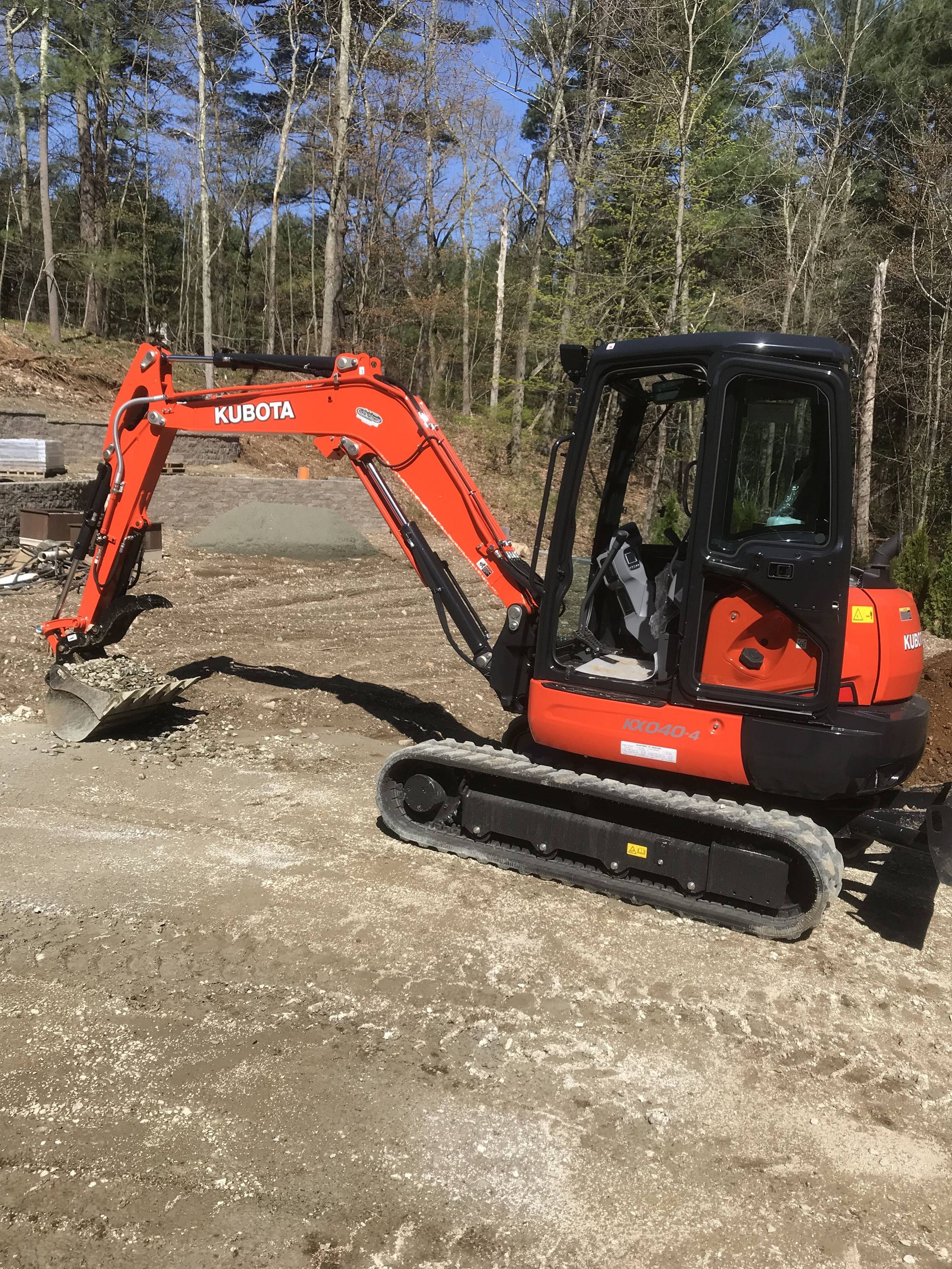 A small red excavator is sitting on top of a dirt field.