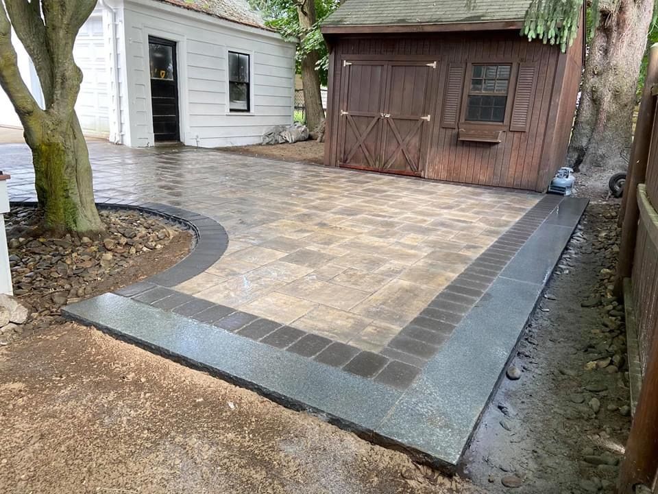 A patio with a shed in the background and a tree in the foreground.